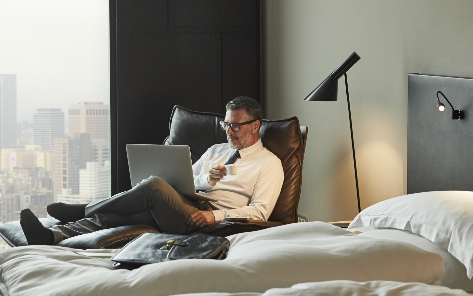 Gambar seorang pria memegang catatan PC dan bersantai di sofa di dalam ruangan.