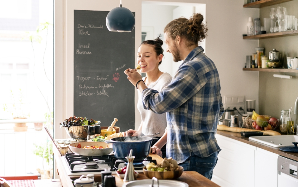 Hình ảnh một người phụ nữ và người đàn ông đang vui vẻ nấu nướng trong phòng ăn.