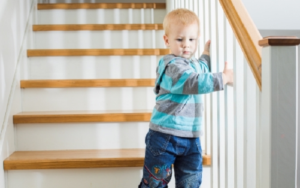 Hình ảnh một đứa trẻ chập chững bên lan can đi xuống cầu thang. 