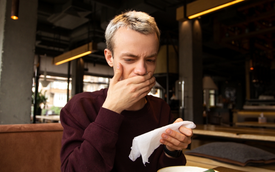 Gambar seorang pelanggan pria menahan mulutnya dan mengerutkan kening karena bau tak sedap di restoran.