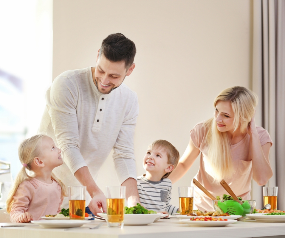 An image of children smiling at the dining table with their parents.