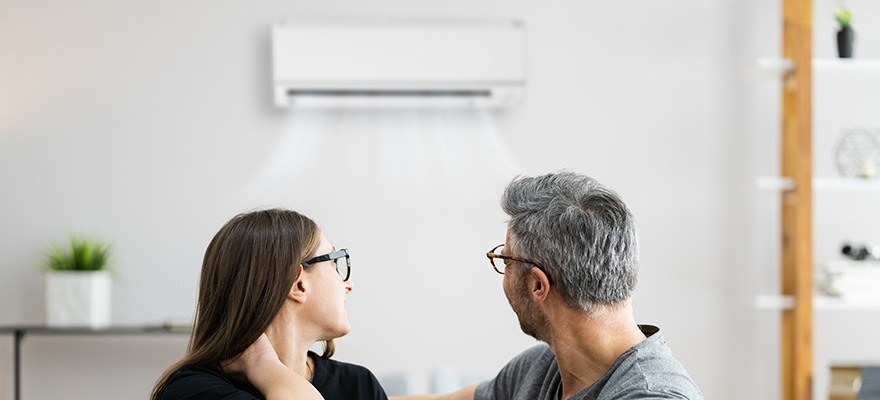 A photo of a women and man sitting on a sofa, looking back at an air conditioner