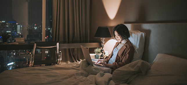 A woman is using a computer on the bed.