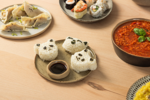 Un plato de Onigiri con forma de panda rodeado de otros platos como sushi y dumplings.