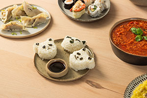 Un plato de Onigiri con forma de panda rodeado de otros platos como sushi y dumplings.