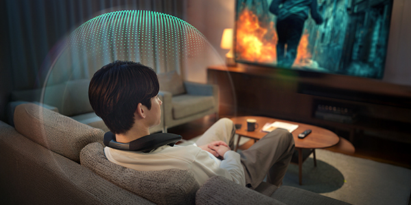 A person sits on a couch wearing a neck speaker while watching TV.