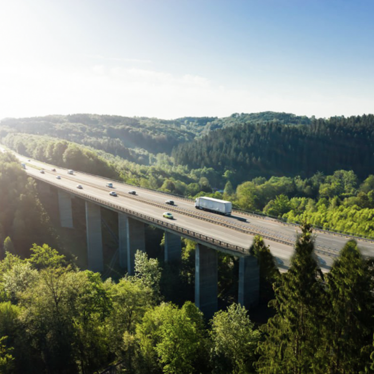 Elevated highway or bridge passing through a lush green area with hills in the background.