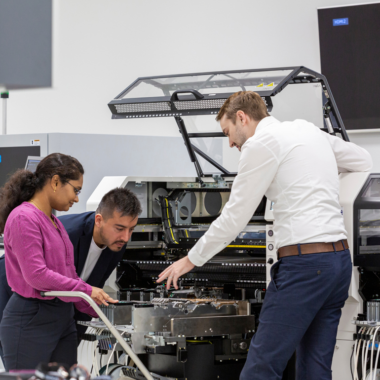 Trois personnes autour d'une grande machine, l'une expliquant quelque chose aux autres
