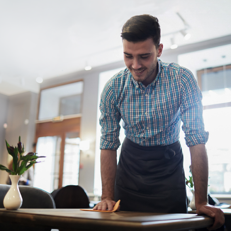 Una persona de pie detrás de una mesa, inclinada hacia delante con las manos sobre la superficie.