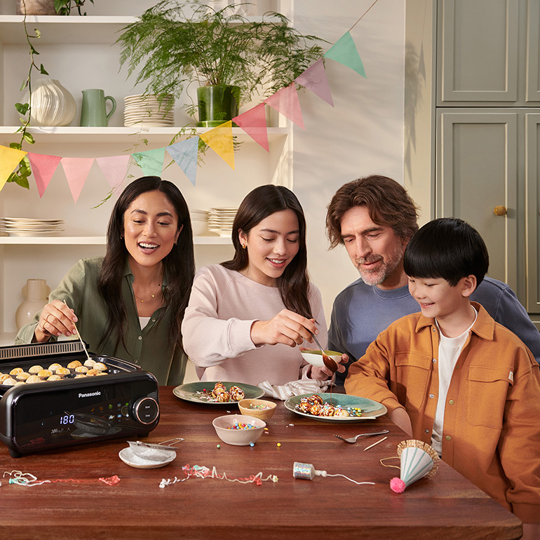 Vier Personen, die an einem Tisch sitzen und mit einem Panasonic Multikocher gemeinsam kochen.