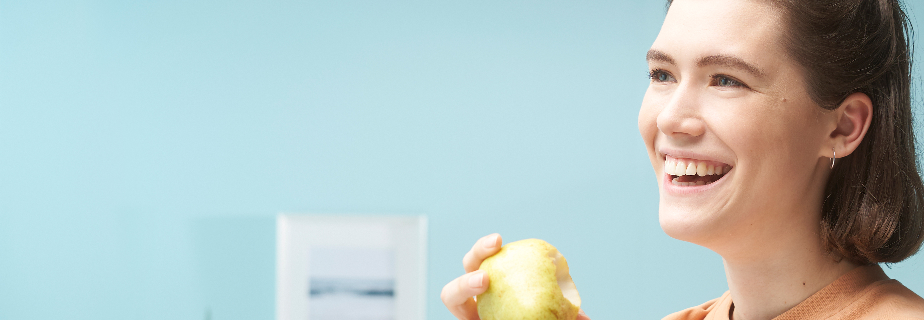 Radosna młoda kobieta z lśniącymi białymi zębami je jabłko