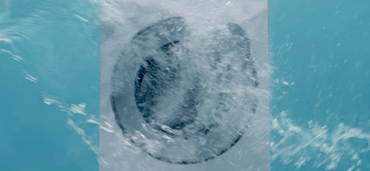 Photo of a front-loading washing machine being heavily splashed by water in a testing environment.