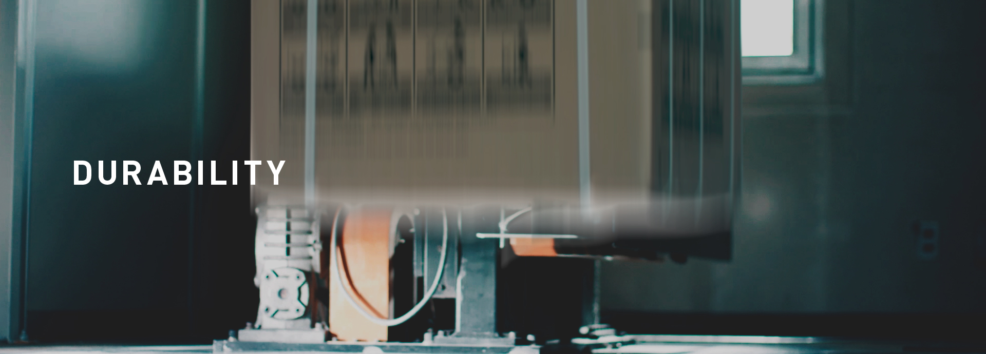 Section Banner: DURABILITY. Photo of a washing machine, boxed and packaged for shipping, being dropped roughly by a machine during testing.