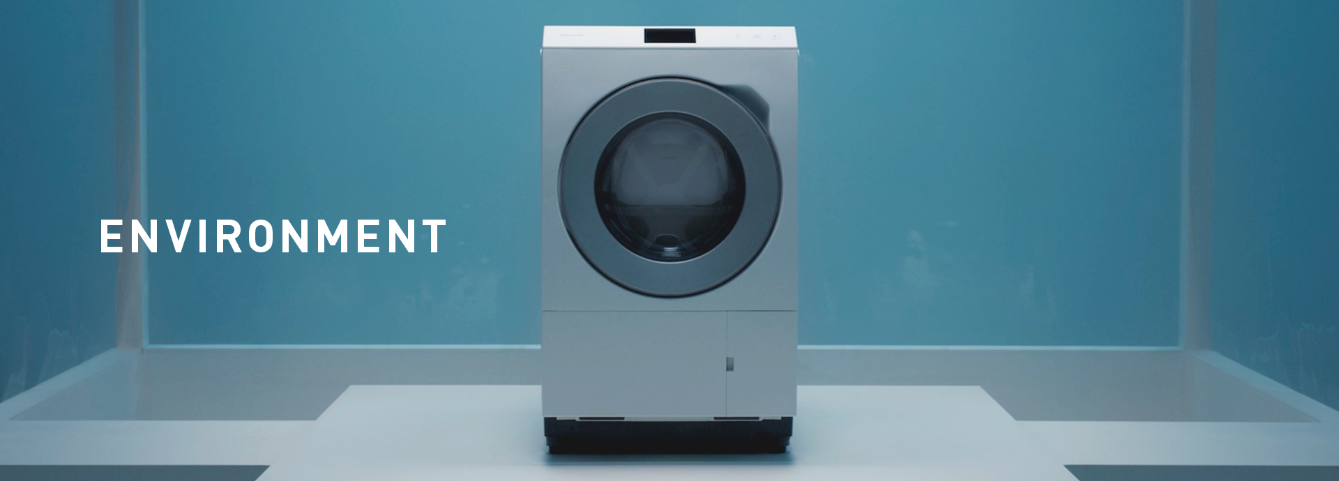 Section Banner: ENVIRONMENT. Photo of a front-loading washing machine in a plastic-sheeted room for quality testing.