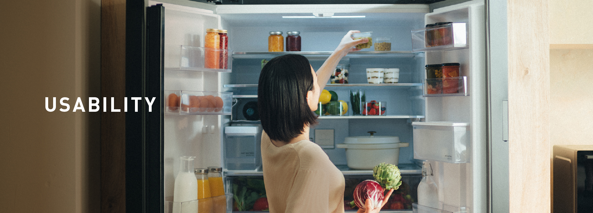 USABILITY. Woman reaching for fresh ingredients in a stylish refrigerator.