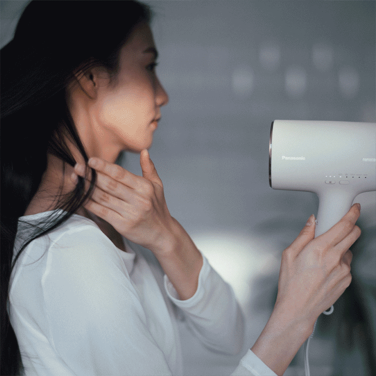 Compact shaver on a bathroom shelf amongst other personal care products. A woman drying her hair with a compact hair dryer.