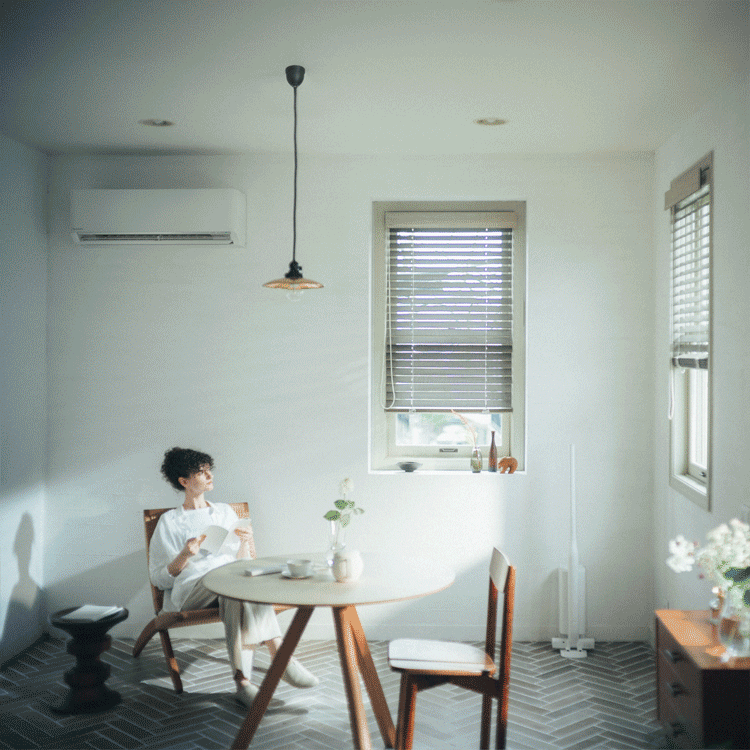 A woman relaxing near an AC unit in a bright room. A woman taking laundry out of a front-loading washing machine.