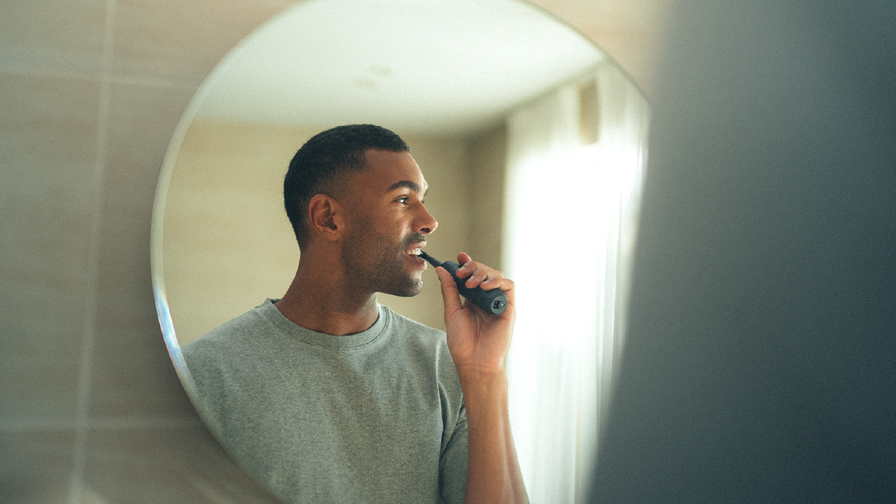 A man brushing his teeth with an electric toothbrush in front of a bathroom mirror.