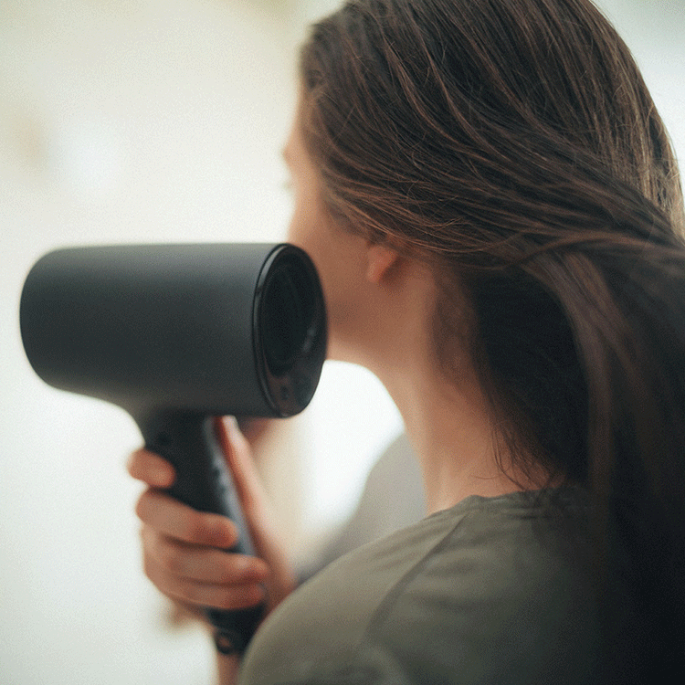 Side-by-side photos: A compact shaver on a small bathroom shelf amongst other personal care products, and a woman drying her long hair with a stylish, compact hair dryer.