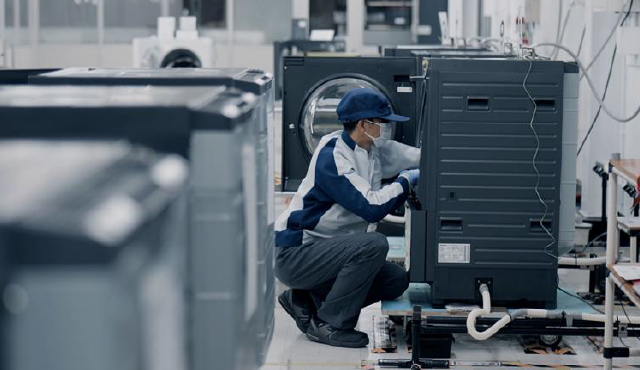Photo of a Panasonic worker inspecting the interior of a front-loading washing machine in a factory.