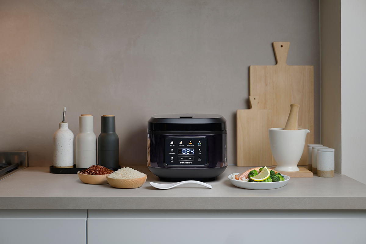 SR-DA152KXE Rice Cooker in Black placed on a kitchen counter, surrounded by cutting boards, cooking utensils, and various ingredients.