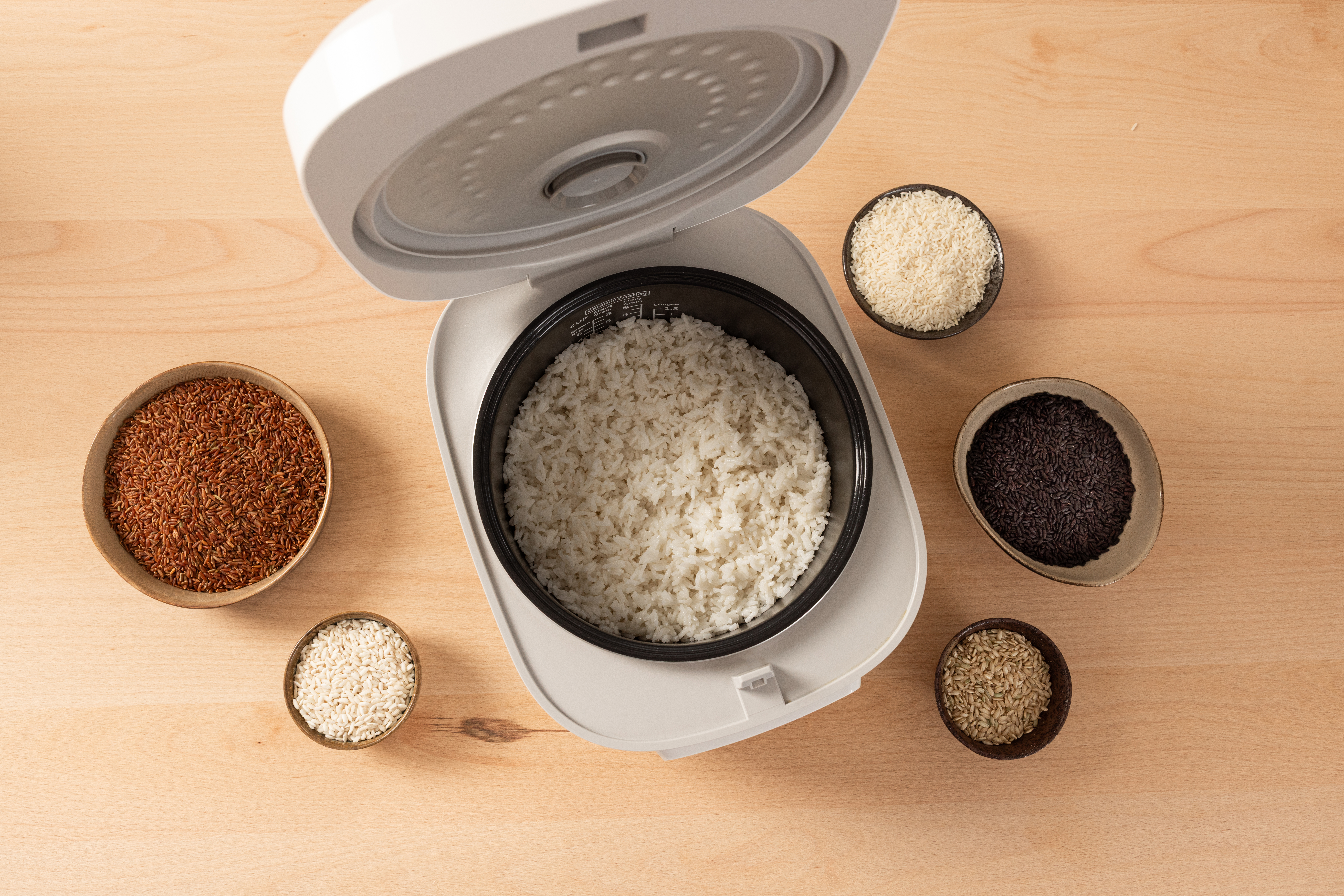 Top view of the SR-DA152WXE Rice Cooker in White, filled with cooked rice and surrounded by small bowls containing different types of rice.
