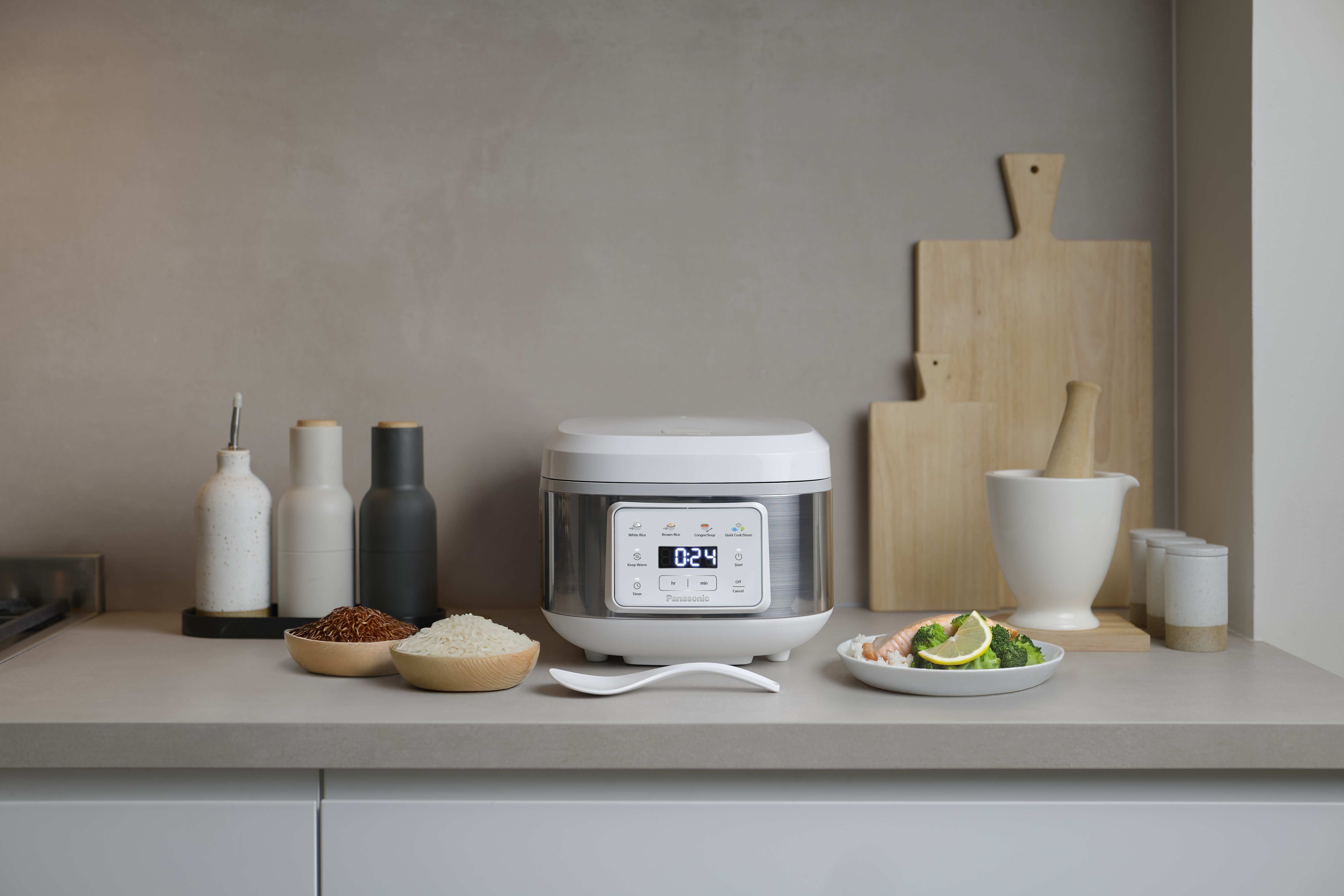 SR-DA152WXE Rice Cooker in White placed on a kitchen counter, surrounded by cutting boards, cooking utensils, and various ingredients.