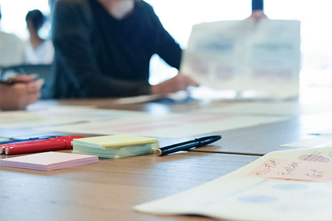 桌面上放置有笔、便签和散落的文件，背景有人在操作