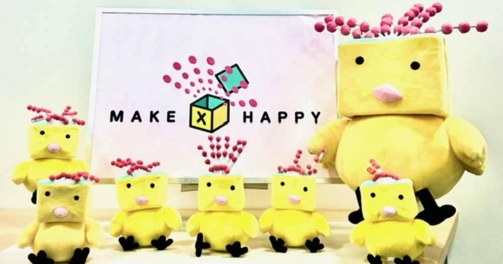 「MAKE HAPPY プロジェクト」のロゴとマスコットキャラクター「はっぴーさん®」の大小のぬいぐるみが並んでいる様子。