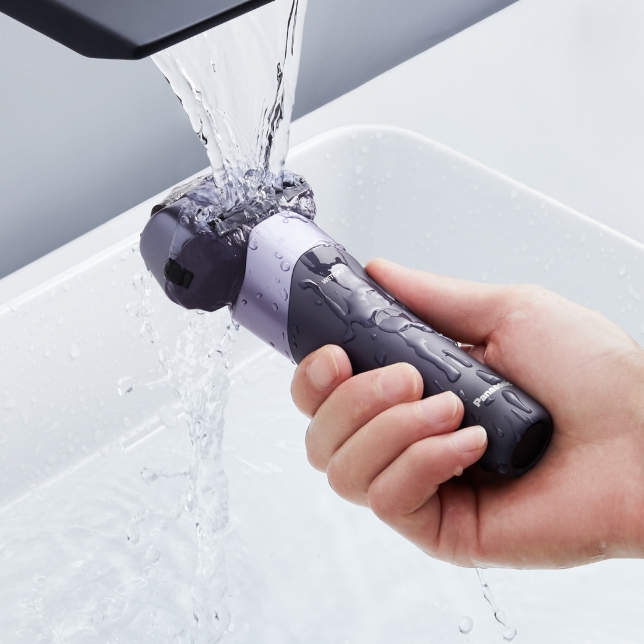 Une main tient le rasoir sous l'eau du robinet pour démontrer l'étanchéité de l'appareil