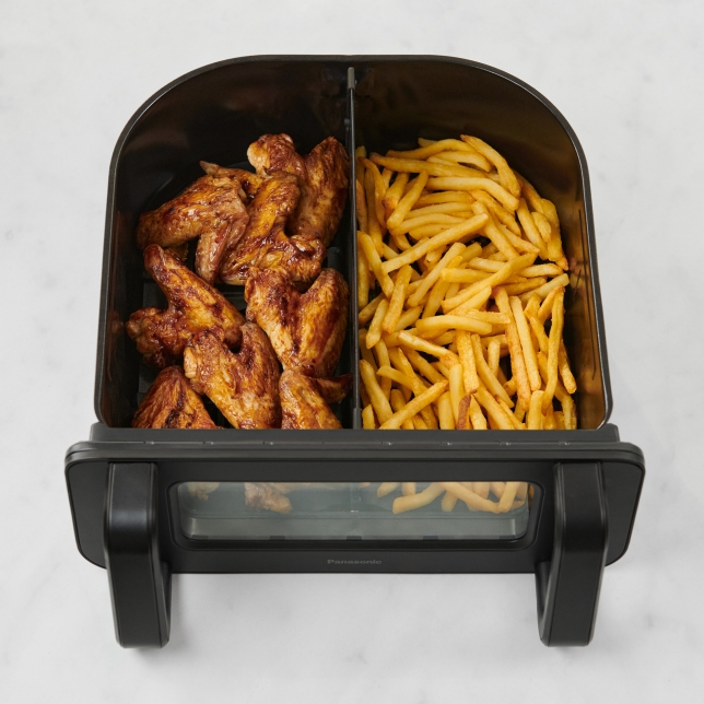 The Panasonic Flex Air Fryer NF-BC1000 is shown on a kitchen countertop from the top with its basket open, revealing chicken wings and fries inside the Dual Baskets.