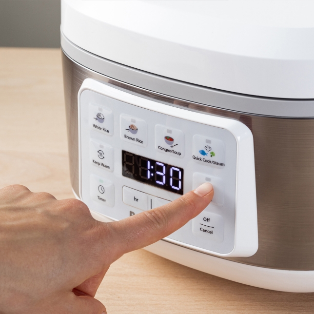 Close-up of the SR-DA152KXE Rice Cooker in Black display showing a countdown timer with a hand selecting a cooking program.