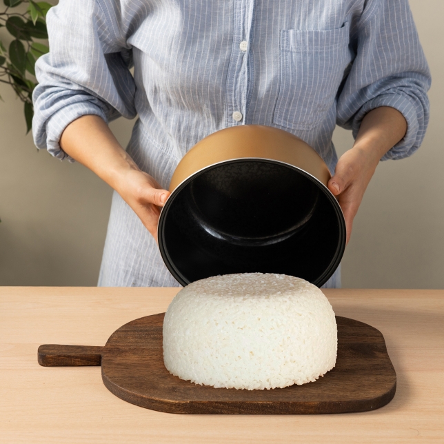 Hands pouring cooked rice from the Rice Cooker Pot onto a cutting board.