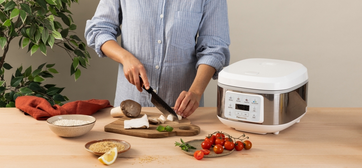A woman cooking beside the SR-DA152WXE Rice Cooker in White, surrounded by various food items while cutting ingredients.