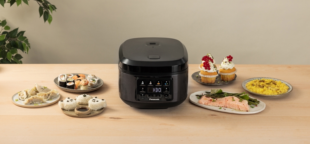 Vista anteriore leggermente rialzata del cuociriso SR-DA152KXE di colore nero con varie pietanze preparate disposte intorno.