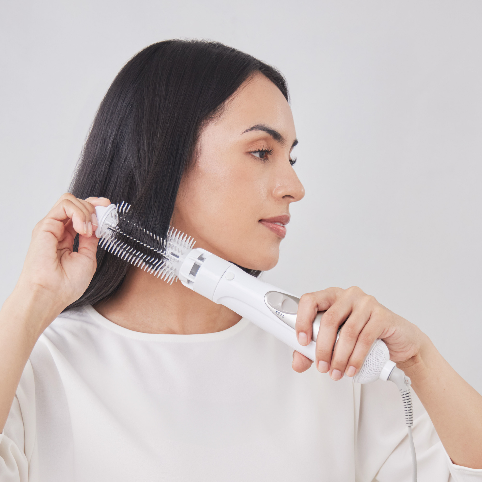 A woman with long, smooth dark hair using Panasonic hair styler with roller brush.
