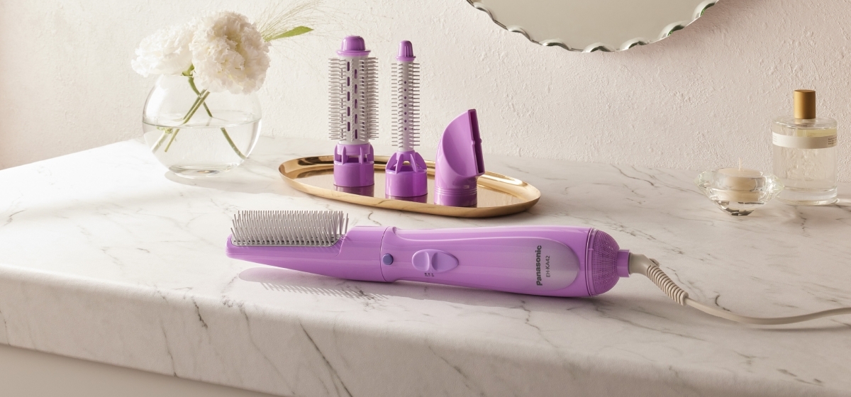A Panasonic hair styler EH-KA42 resting on a marble countertop. Three other purple attachments are arranged on a gold tray behind it.