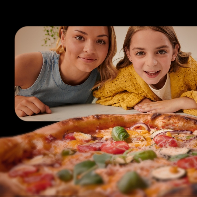 Två flickor tittar på en nygräddad pizza i Panasonic Flex Air Fryer NF-BC1000, sett inifrån apparaten