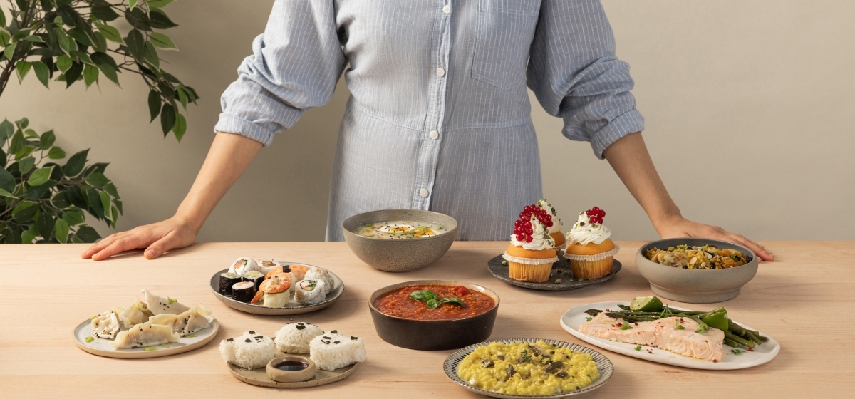 Vy ovanifrån av den vita riskokaren SR-DA152WXE, fylld med kokt ris och omgiven av små skålar med olika typer av ris.