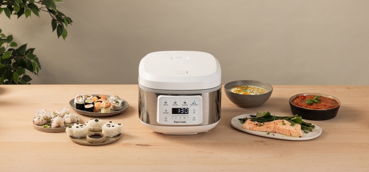 Något upphöjd vy framifrån av den vita riskokaren SR-DA152WXE med olika tillagade rätter arrangerade runt den.