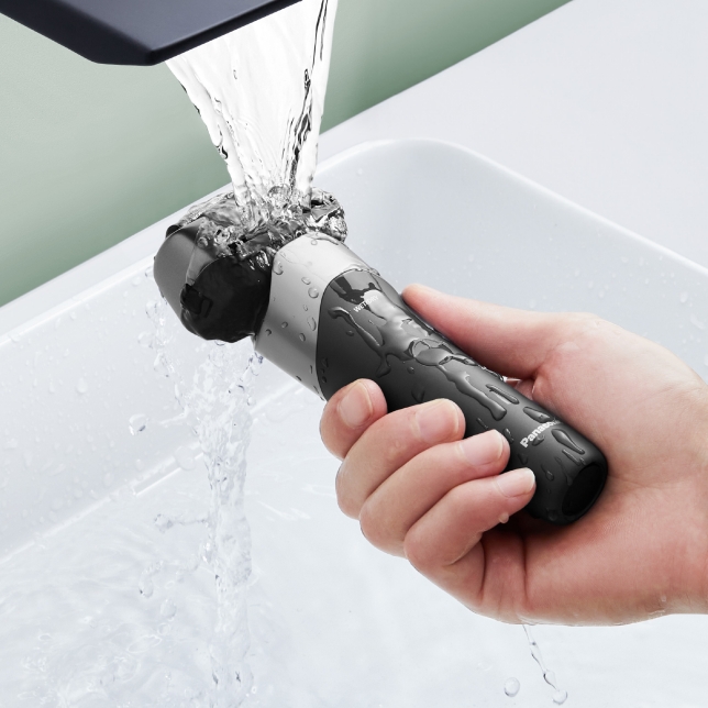 A hand holding the shaver under running water to demonstrate the waterproof design